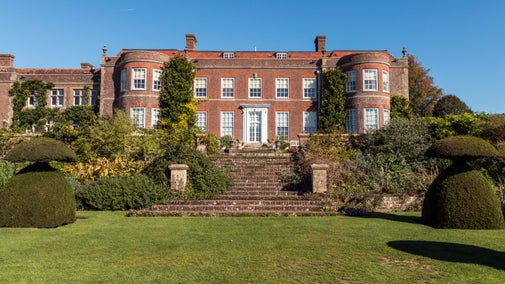 The house at Hinton Ampner, Hampshire, with stone steps leading up to it from a lawn, with topiary trees on either side